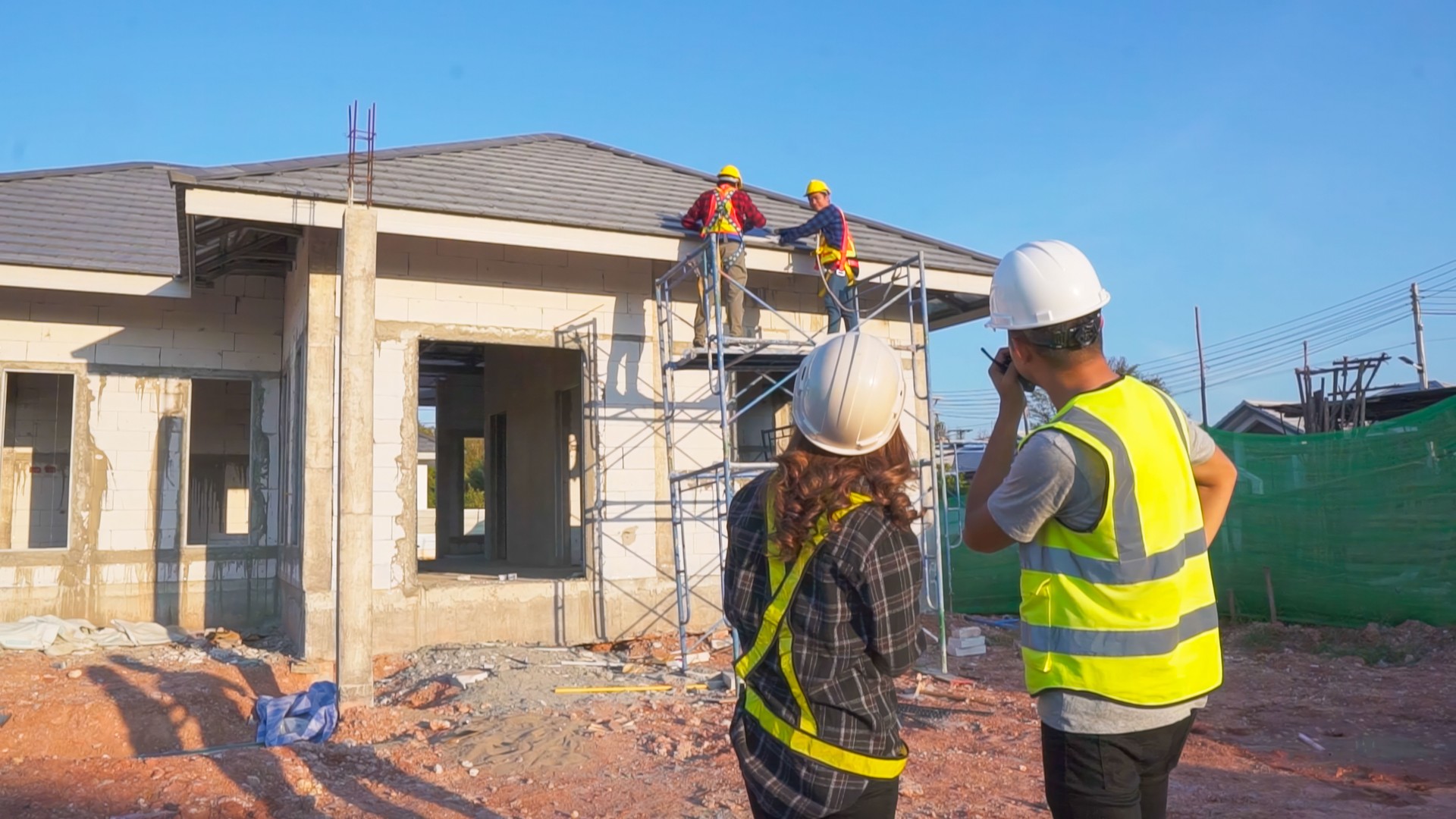 Asian male construction engineer talking to Asian female architects. standing at a construction site to explain install solar cells on the roof of the house.